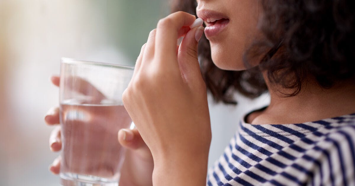 A woman takes a pill with a glass of water.