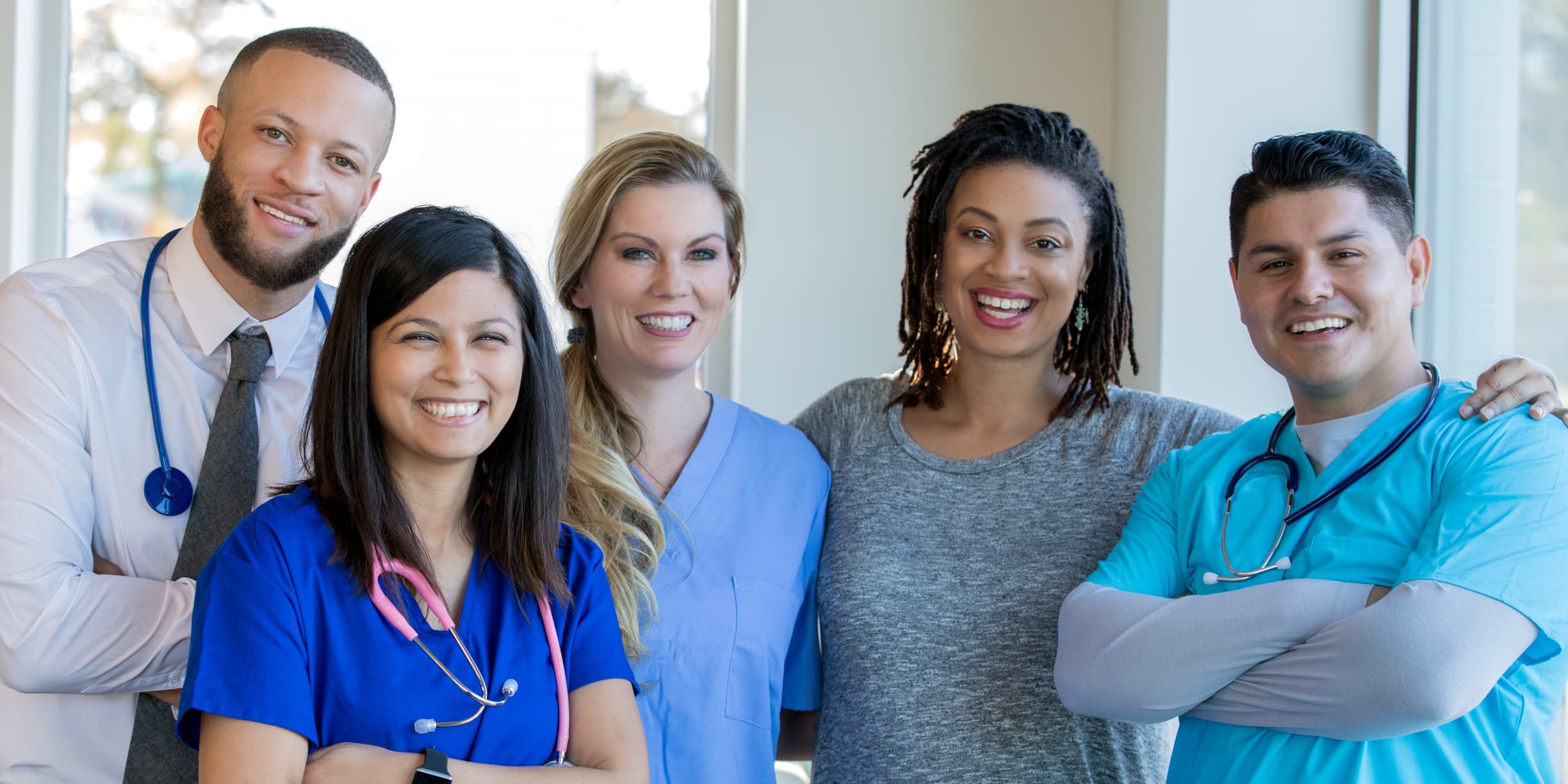 Diverse group of nurses, doctors, and other healthcare professionals are standing together confidently in a hospital hallway.