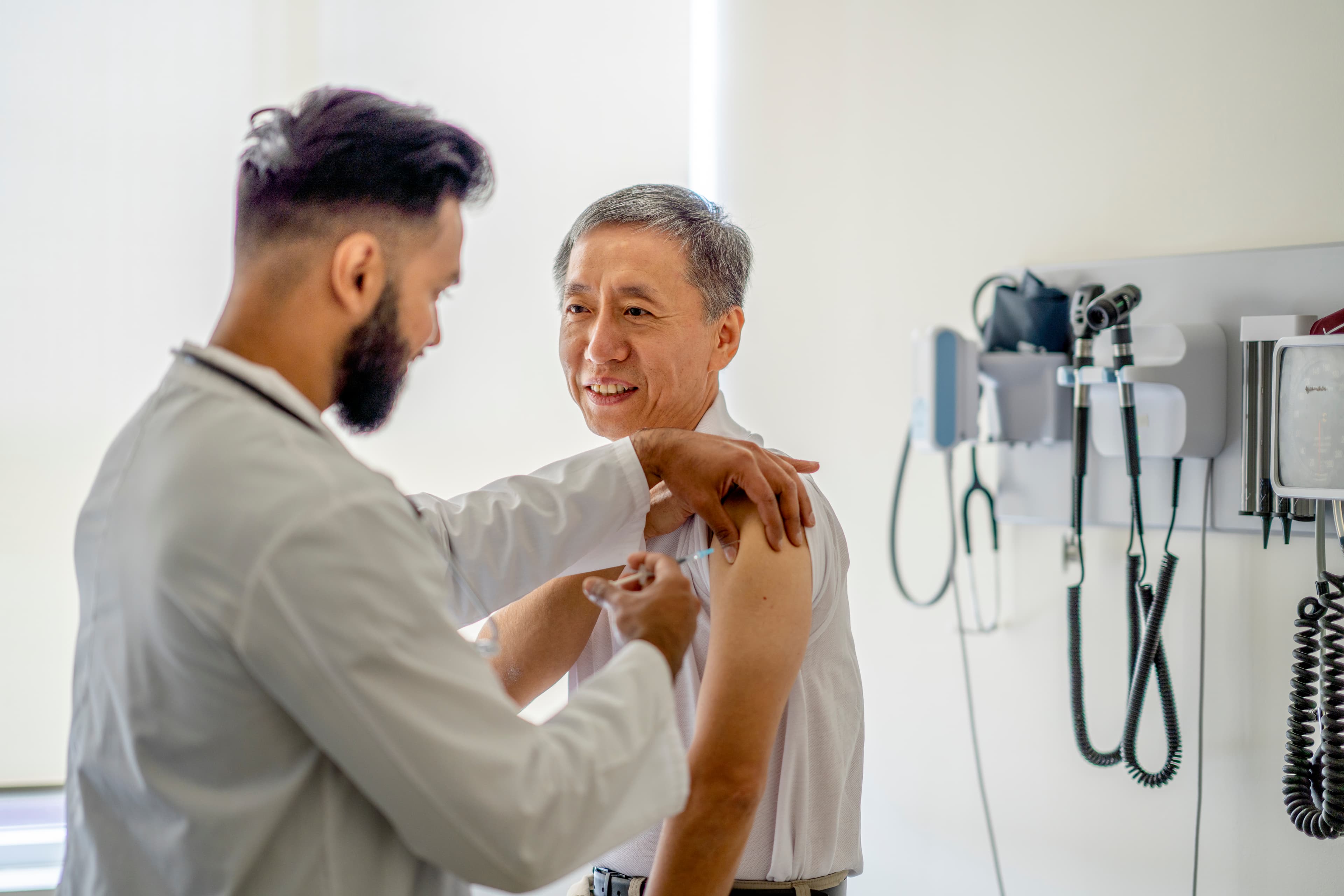 A senior man is receiving a medical injection on his right arm. A male doctor is administering the injection into his arm.