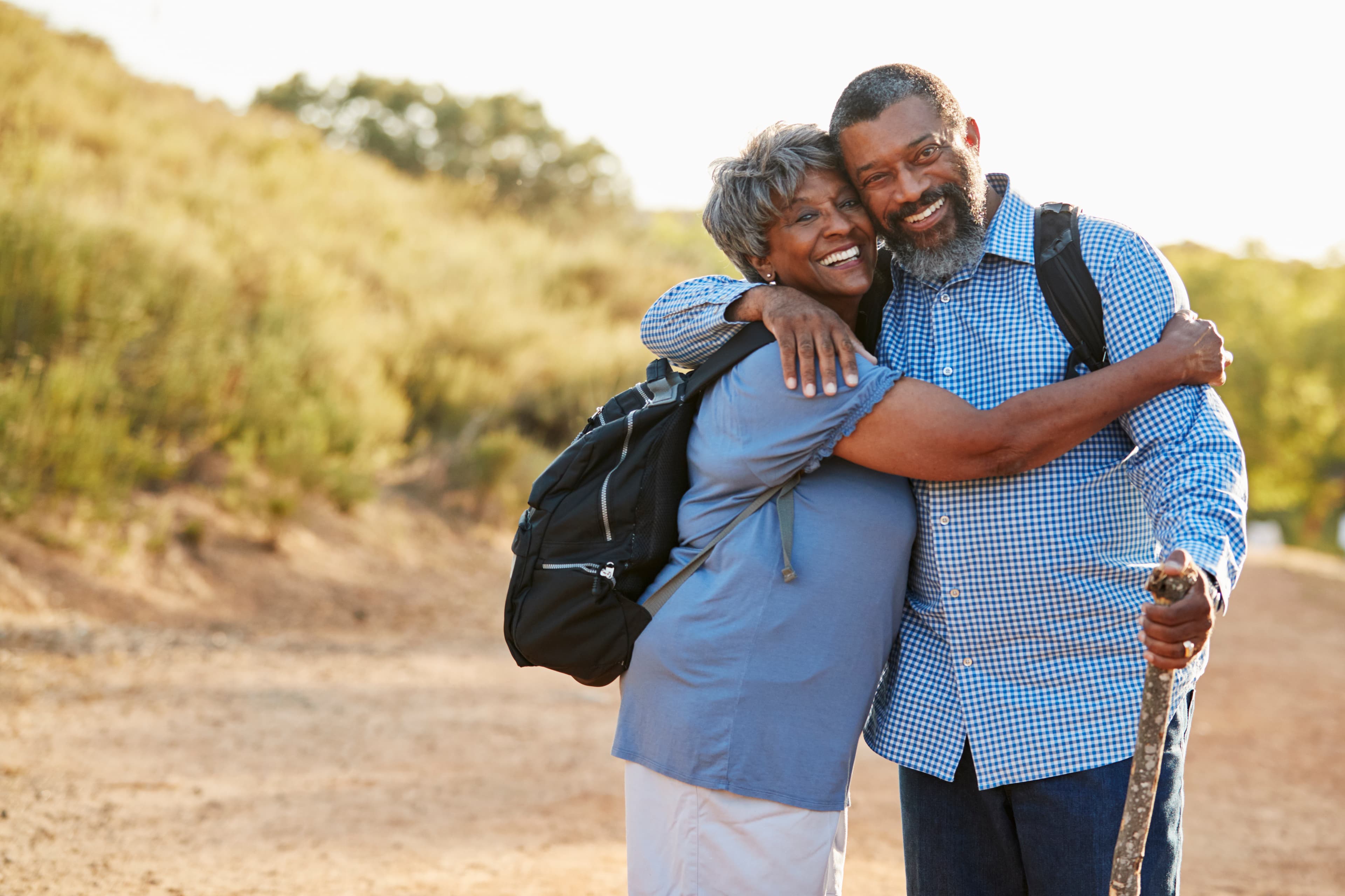 Portrait Of Senior Couple Wearing Backpacks Hiking In Countryside Together