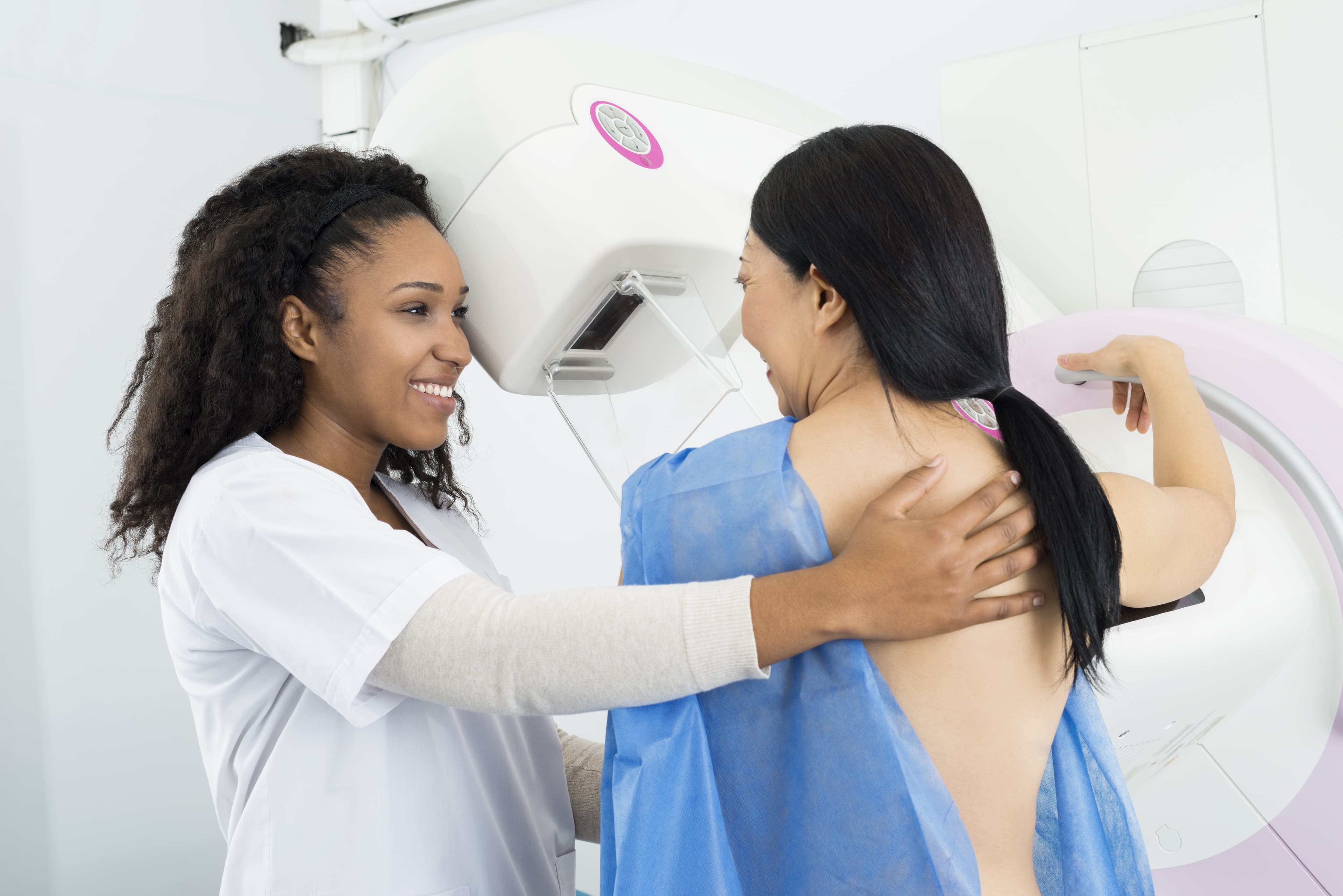 Happy female doctor assisting mature woman undergoing mammogram X-ray test in hospital