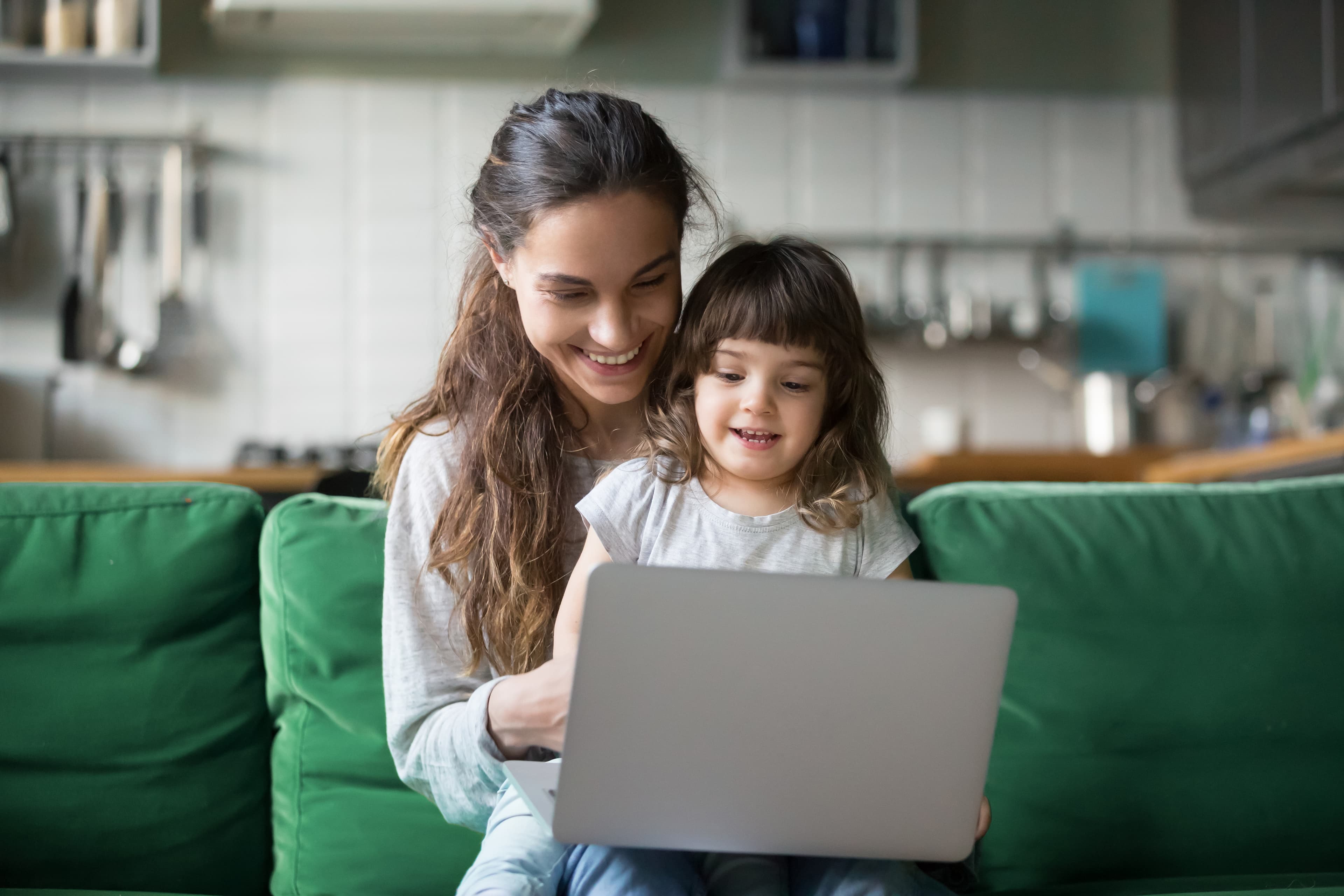 Happy laughing single mother and little preschool cute daughter using laptop online application, making video call, having fun, babysitter teaching small girl use computer, watching cartoons together