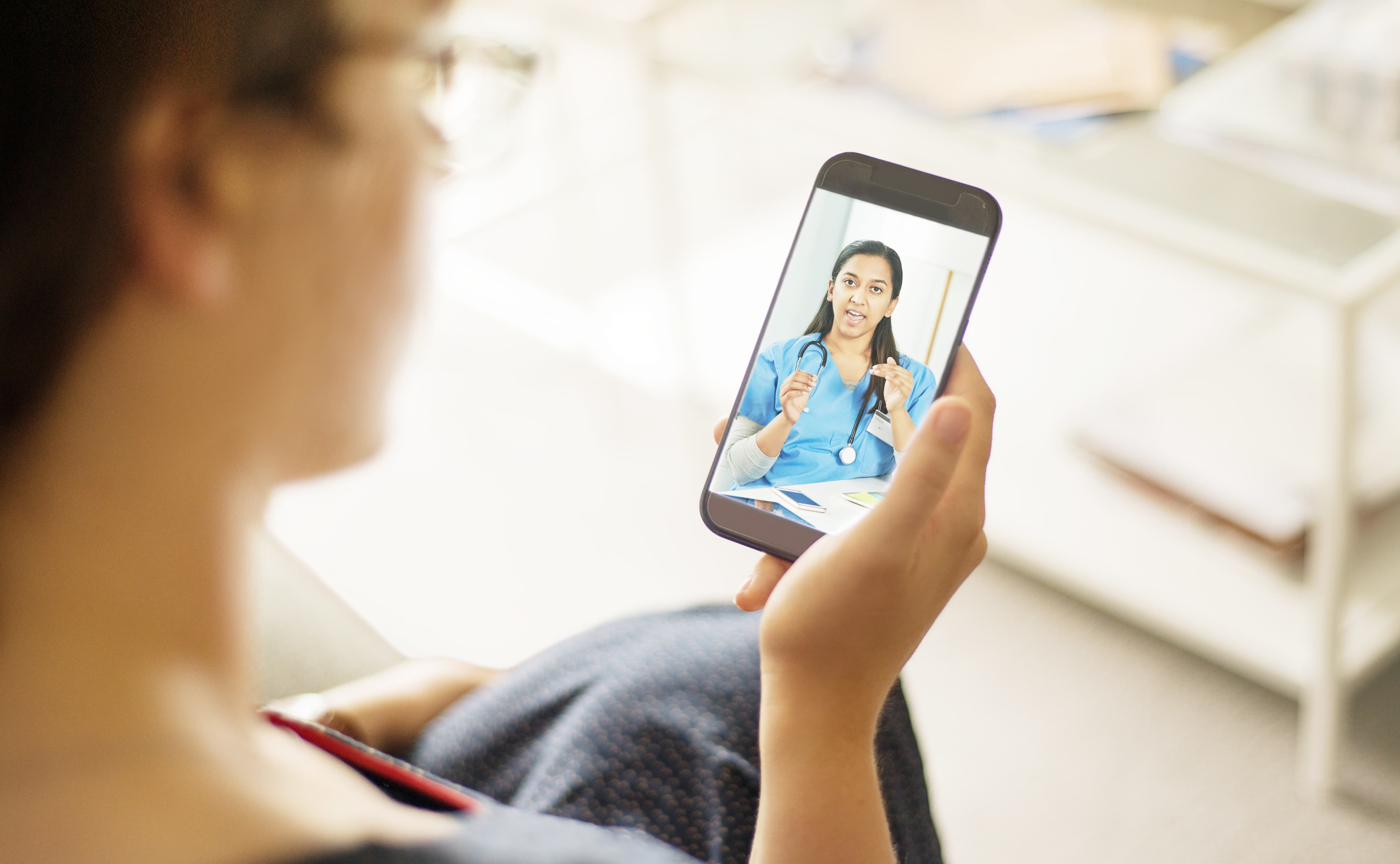 Over the shoulder shot of a patient talking to a doctor using of a mobile phone