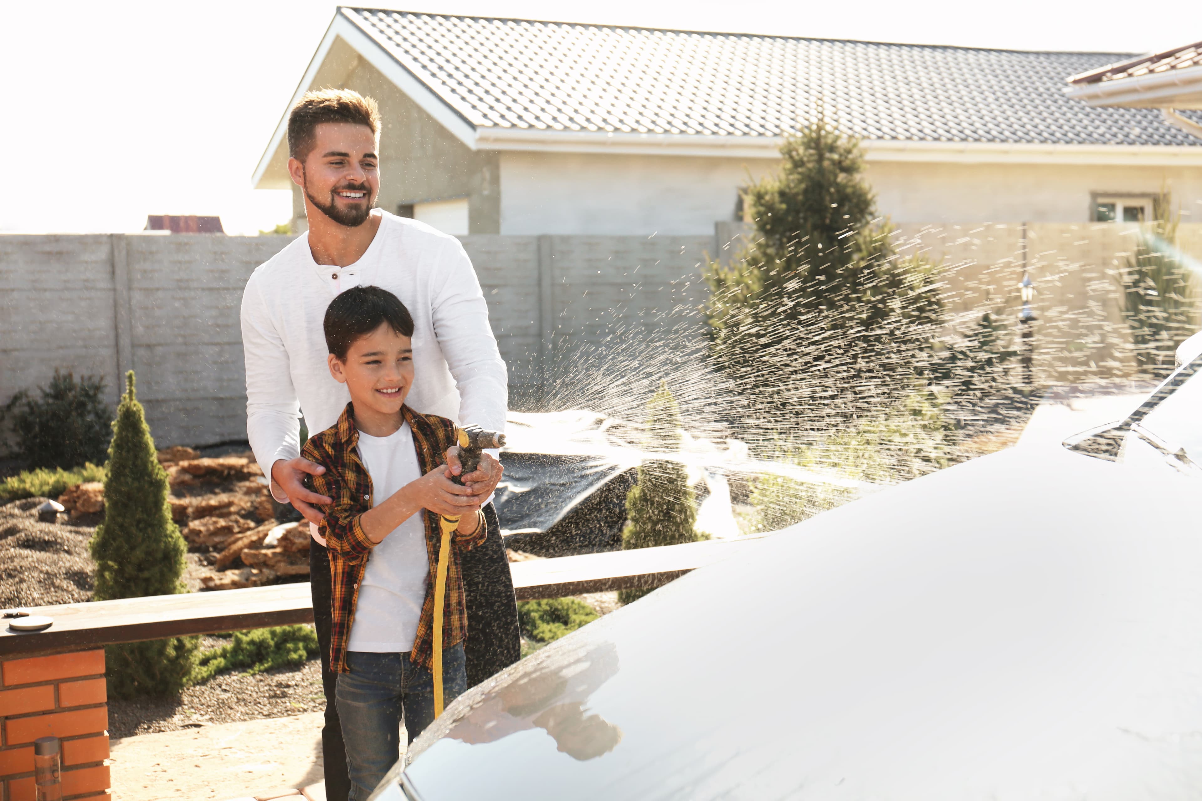 Dad and son washing car at backyard on sunny day