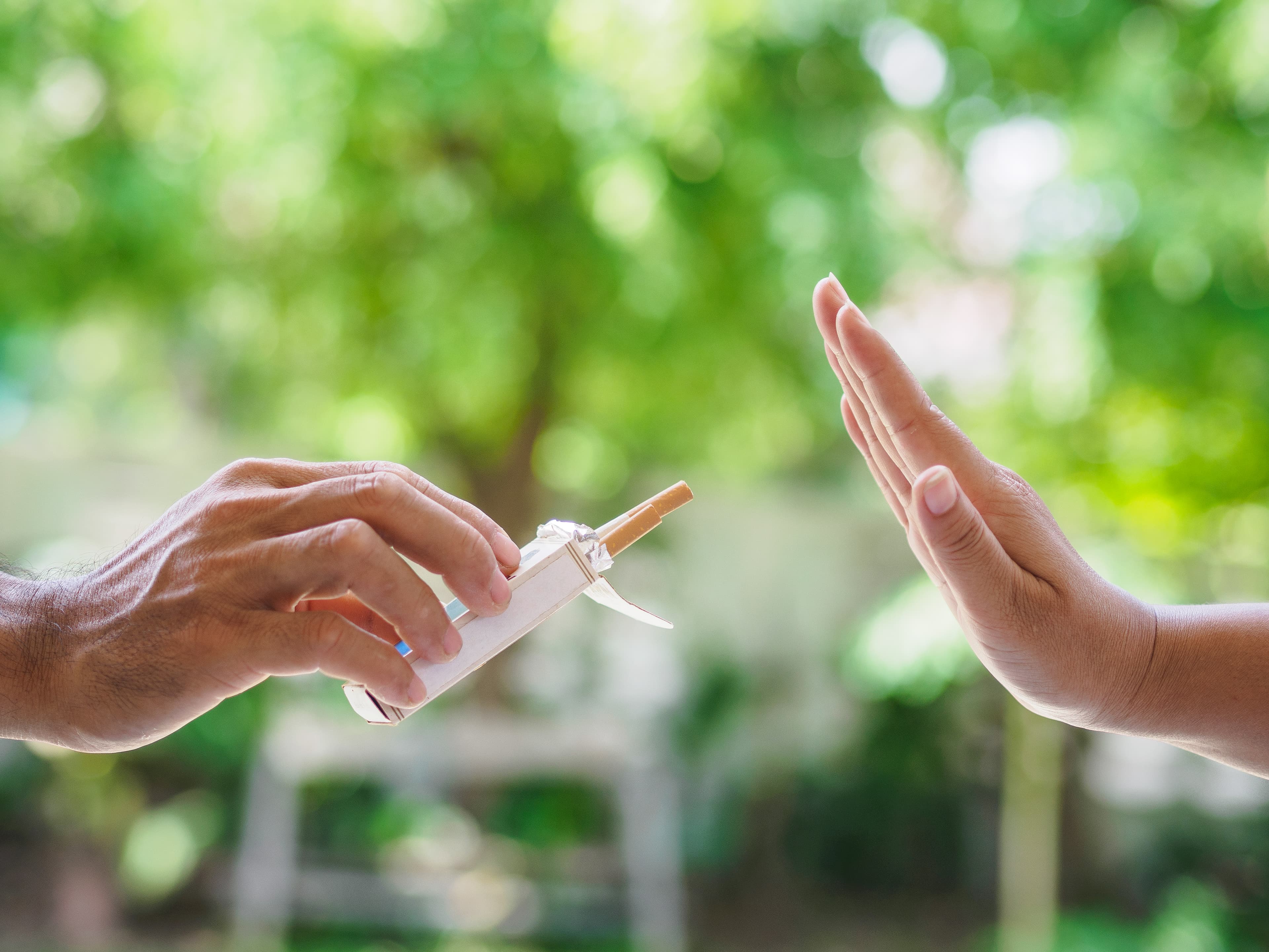 No smoking. Close up of male hands holding cigarettes and proposing it to person. The human arm is gesturing with refusal on bokeh background.