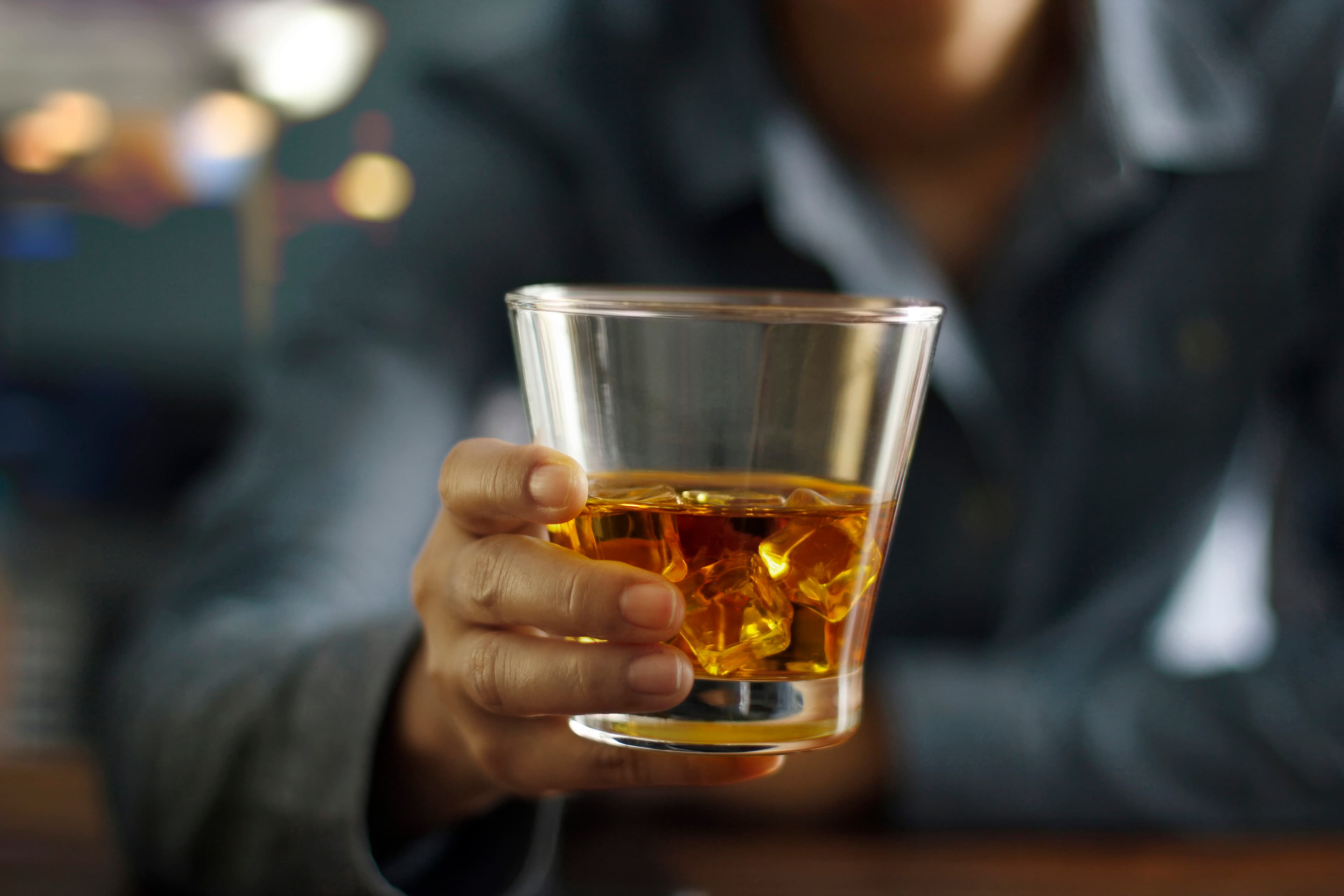 Close-up men holding whiskey drink alcoholic beverage at bar counter in the pub background.