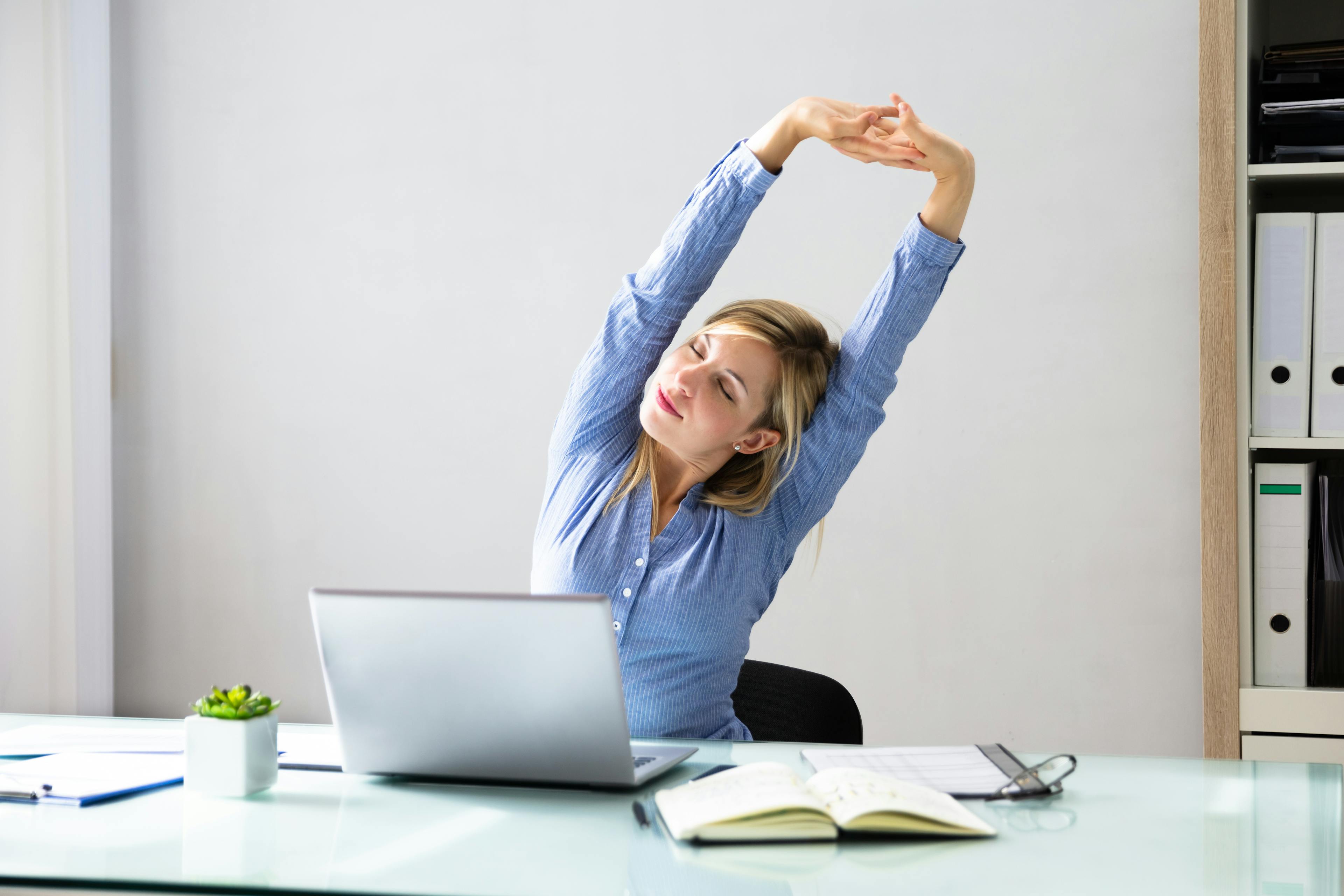 Young Businesswoman Stretching Her Arms With Laptop On Desk