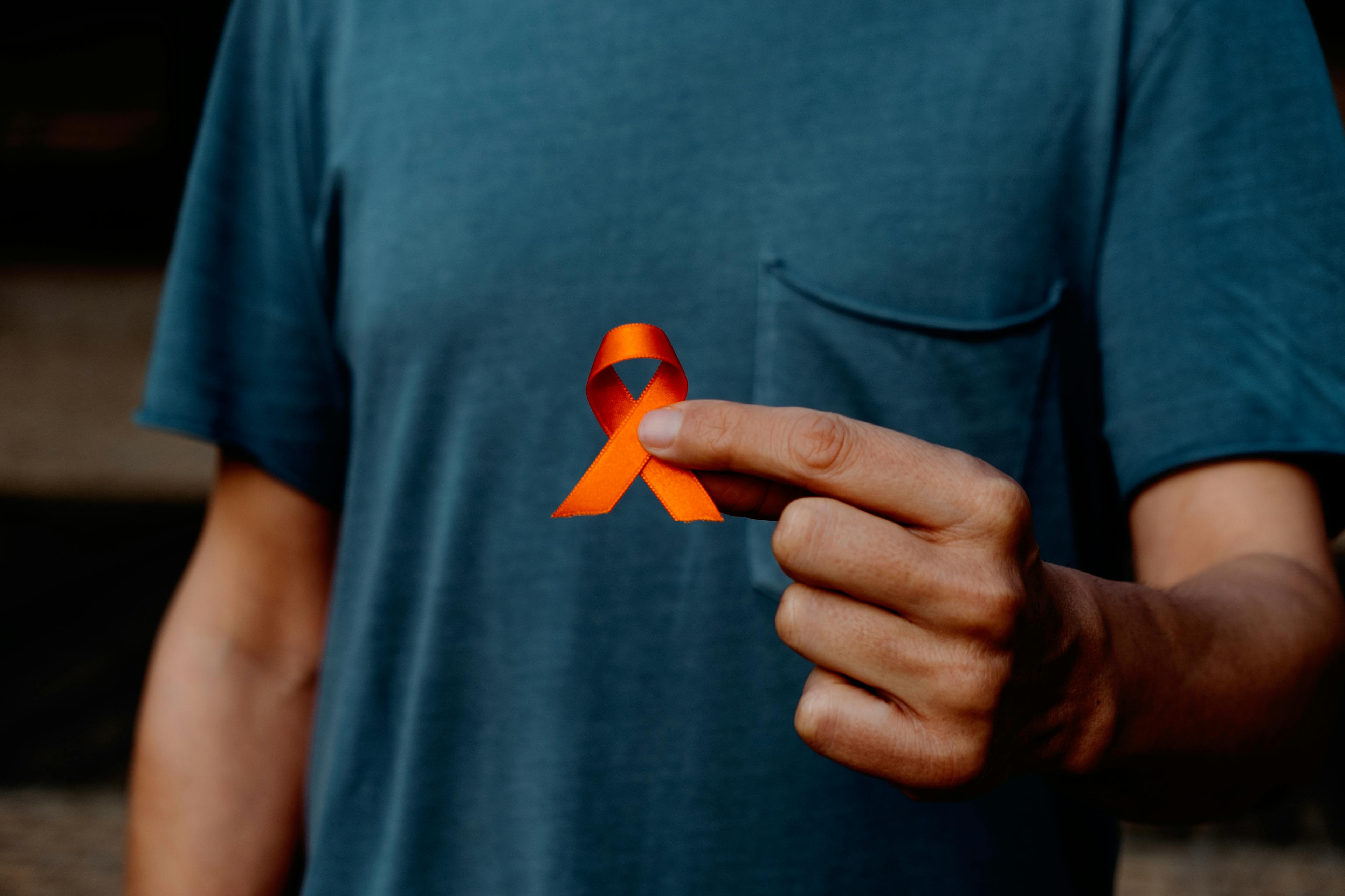 closeup of a young caucasian man, wearing a gray t-shirt, with an orange ribbon in his hand, in support of people affected by multiple sclerosis