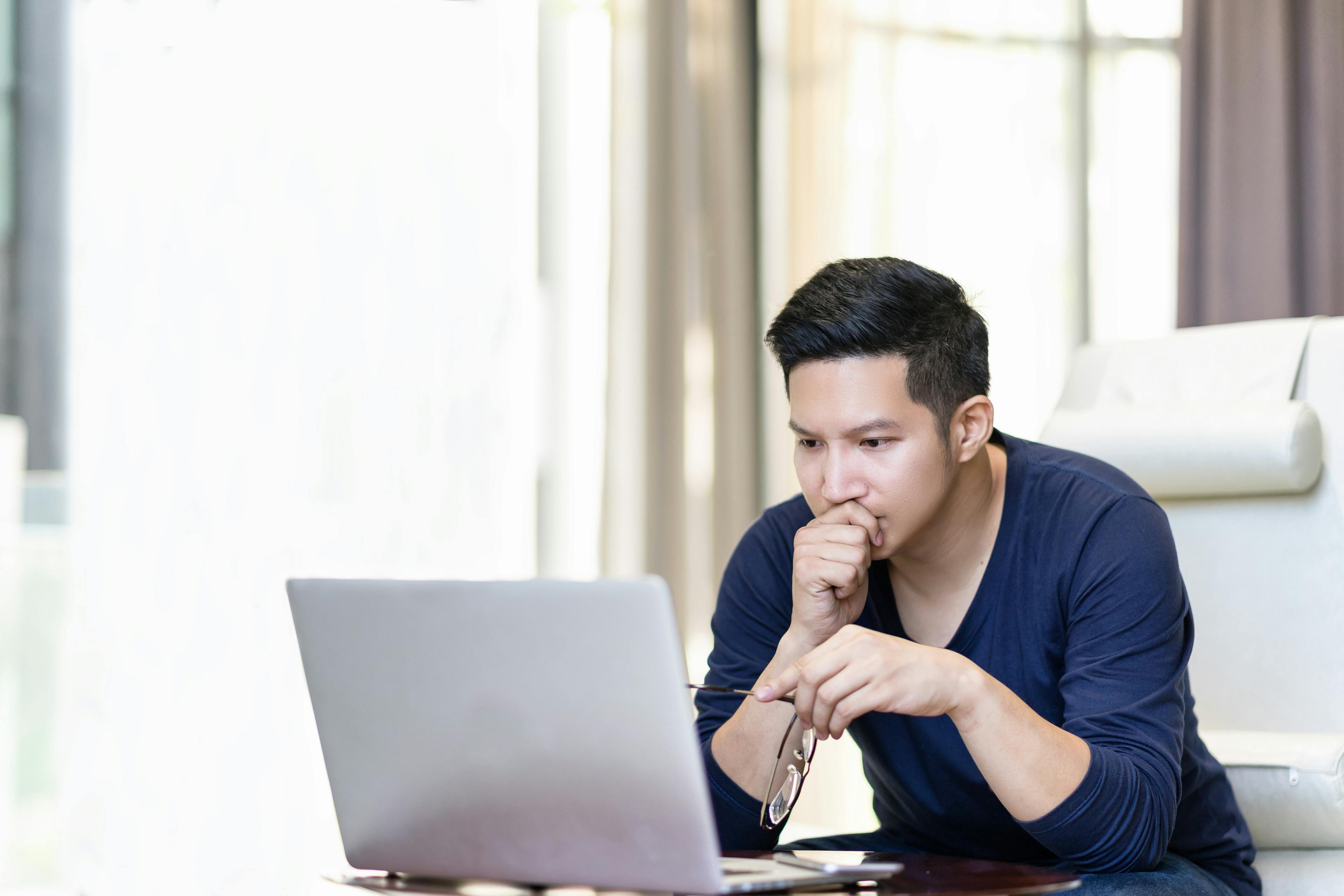seriously confident asian young freelancer in smart casual working and concentrated on laptop sitting on desk in modern office ,co-working space or at home with copy space, webinar over the internet