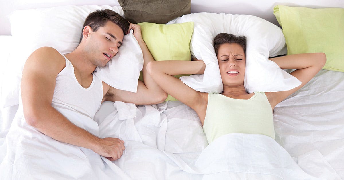 A woman covers her ears as a man snores beside her in bed