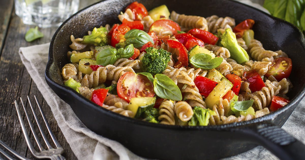 A cast iron pan filled with spiral pasta, tomatoes, broccoli and fresh herbs. 