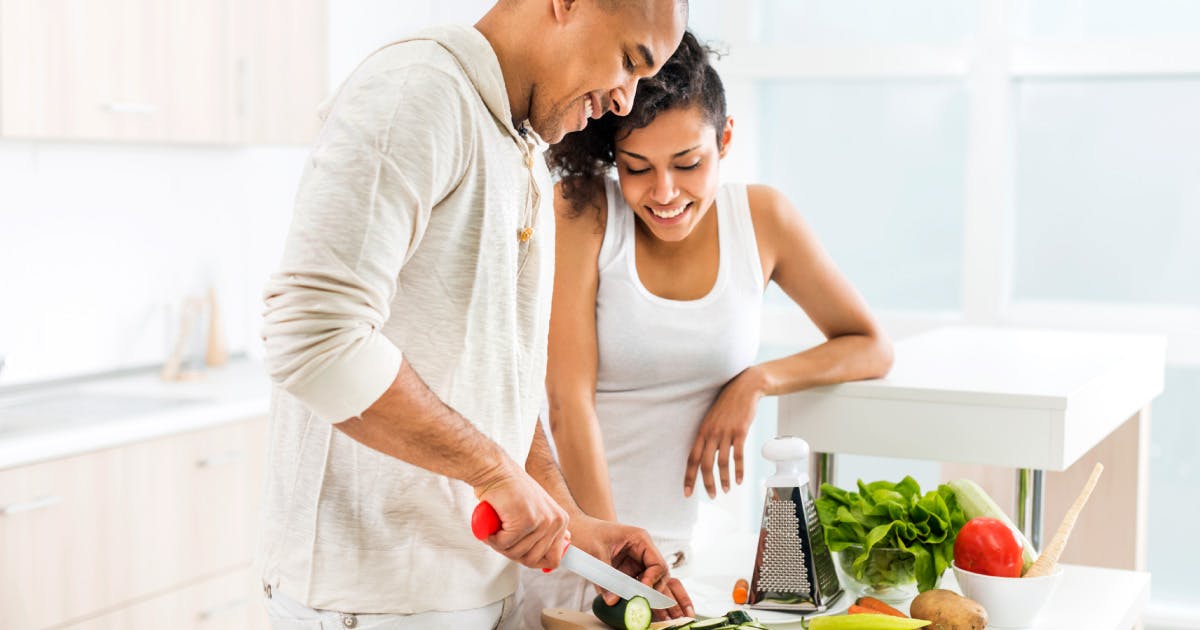 A couple cutting fresh vegetables at a kitchen counter.