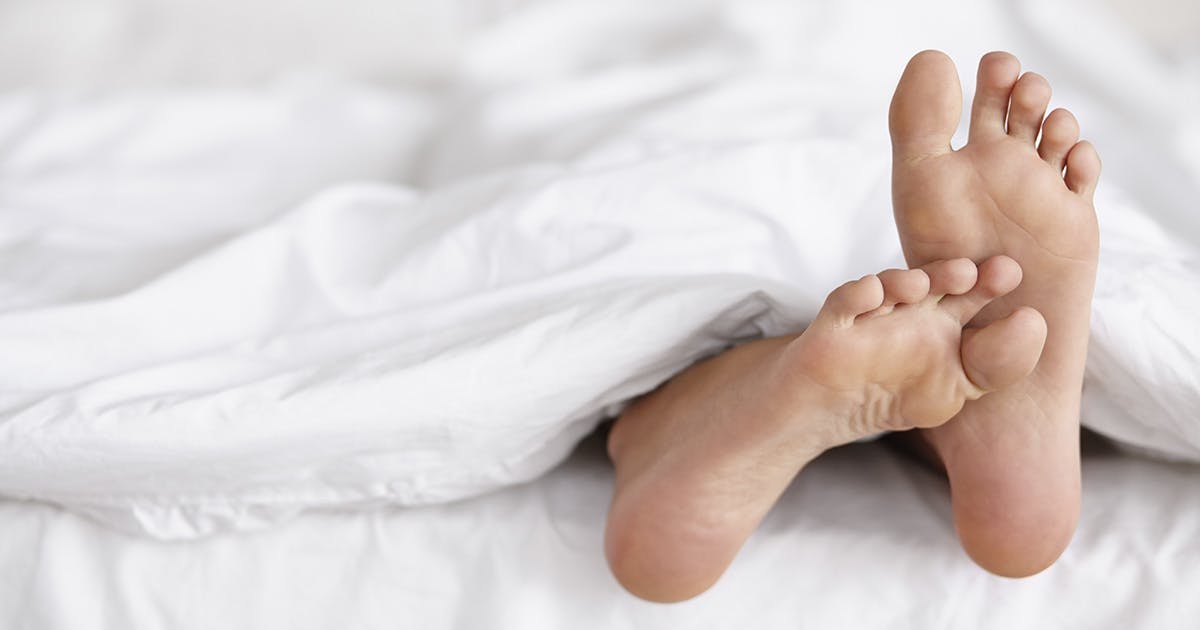 A pair of feet stick out from under bed sheets