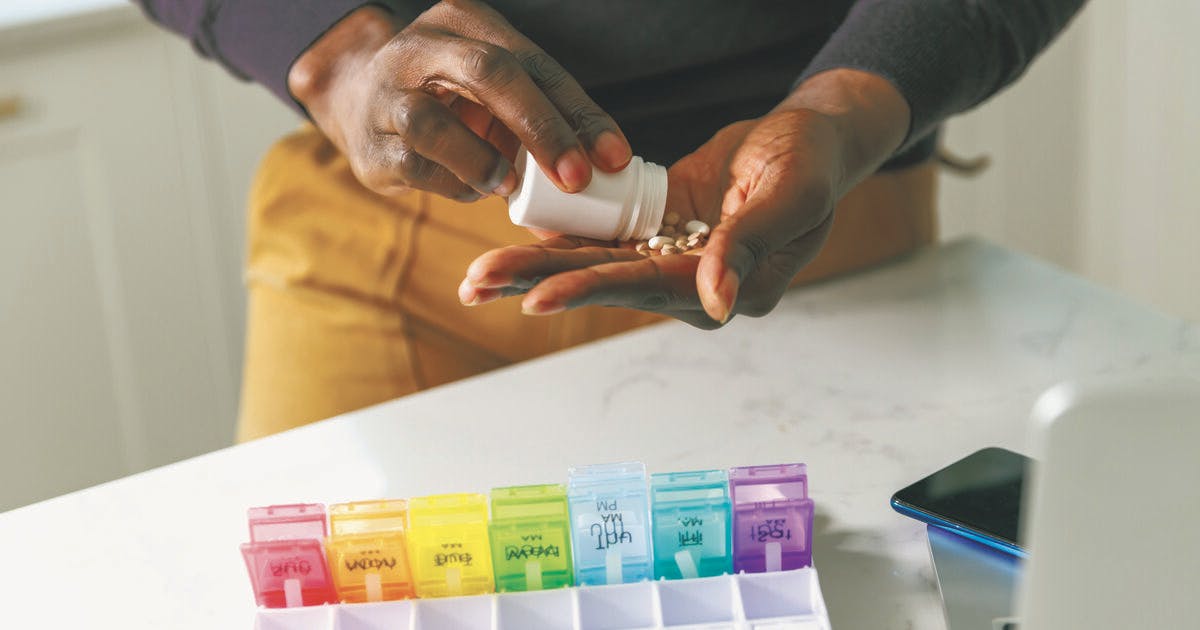 Hands shake pills from a bottle to place in a weekly organizer.