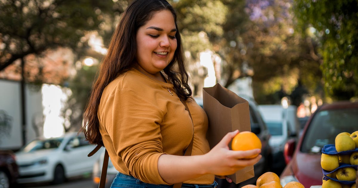 A woman selects an orange at a sidewalk fruit stand.