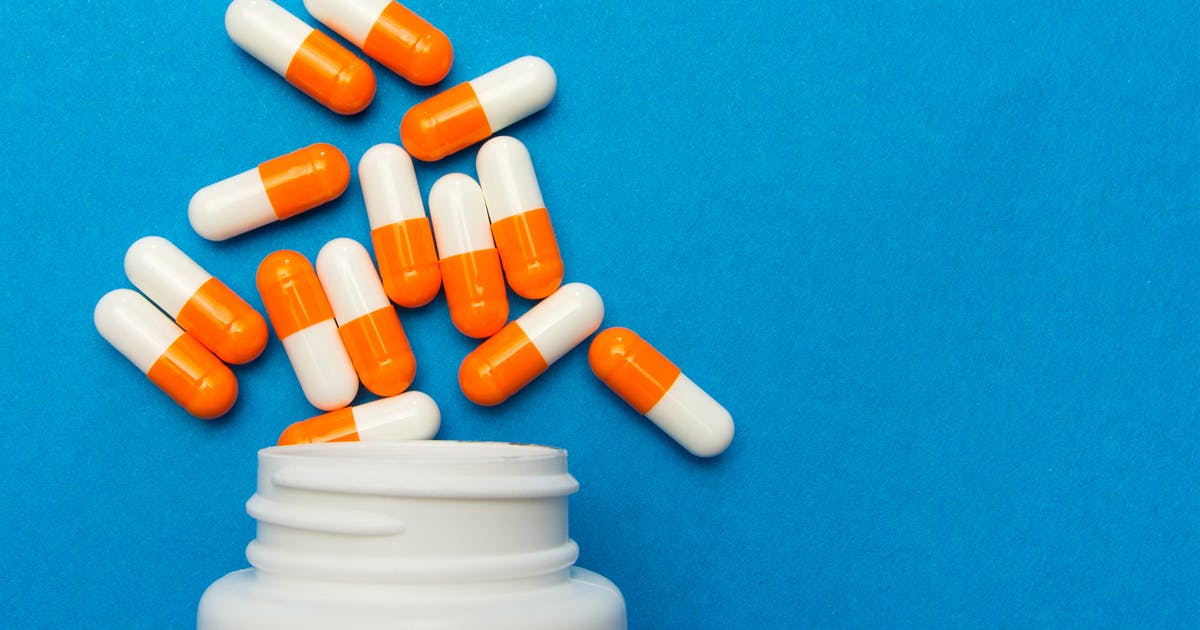 Orange and white capsules spill out of a white bottle onto a blue background