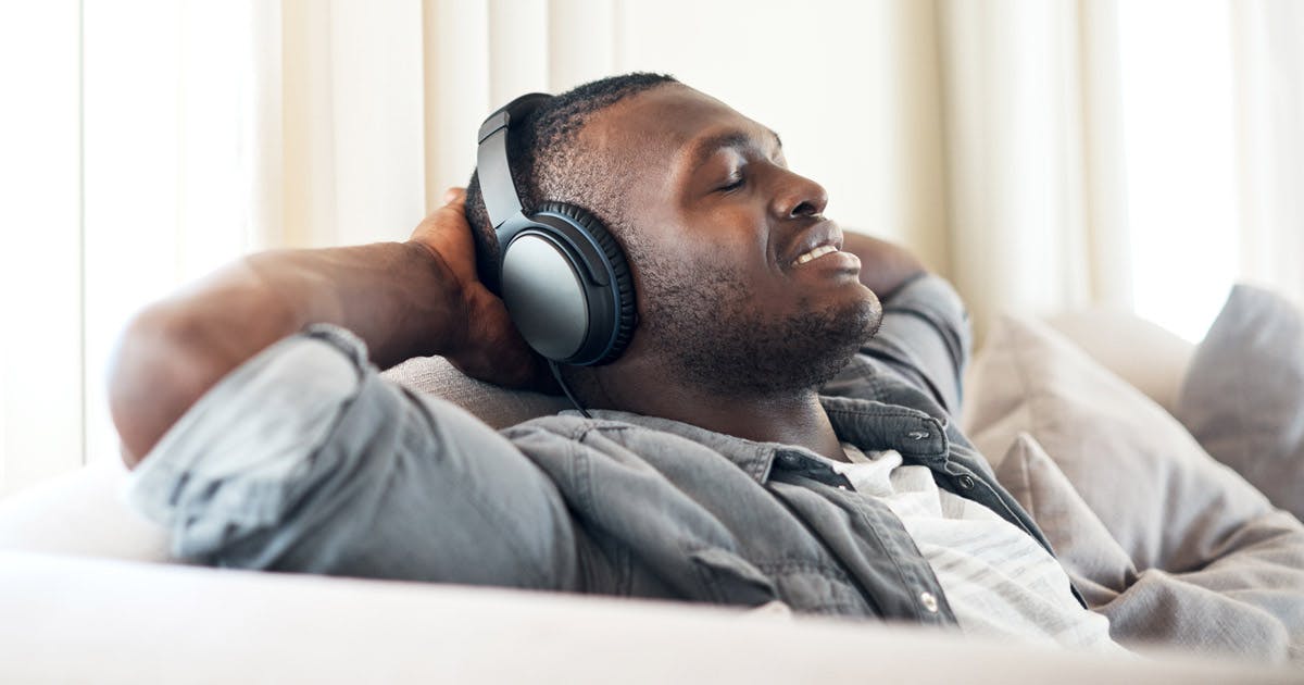 A relaxed man sitting on a couch with eyes closed and headphones on.
