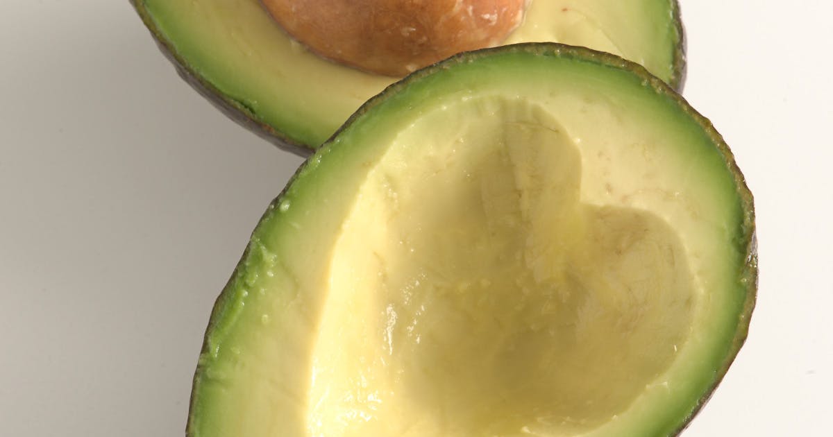 Two halves of a sliced avocado. The side without the pit is scooped in the shape of a heart.