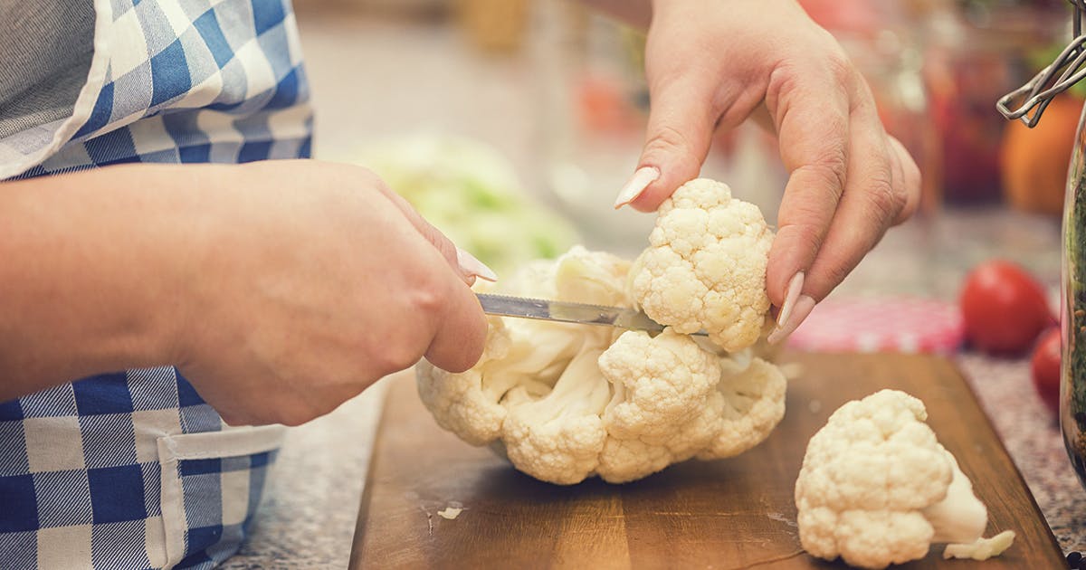 A pair of hands chop cauliflower on a cutting board.