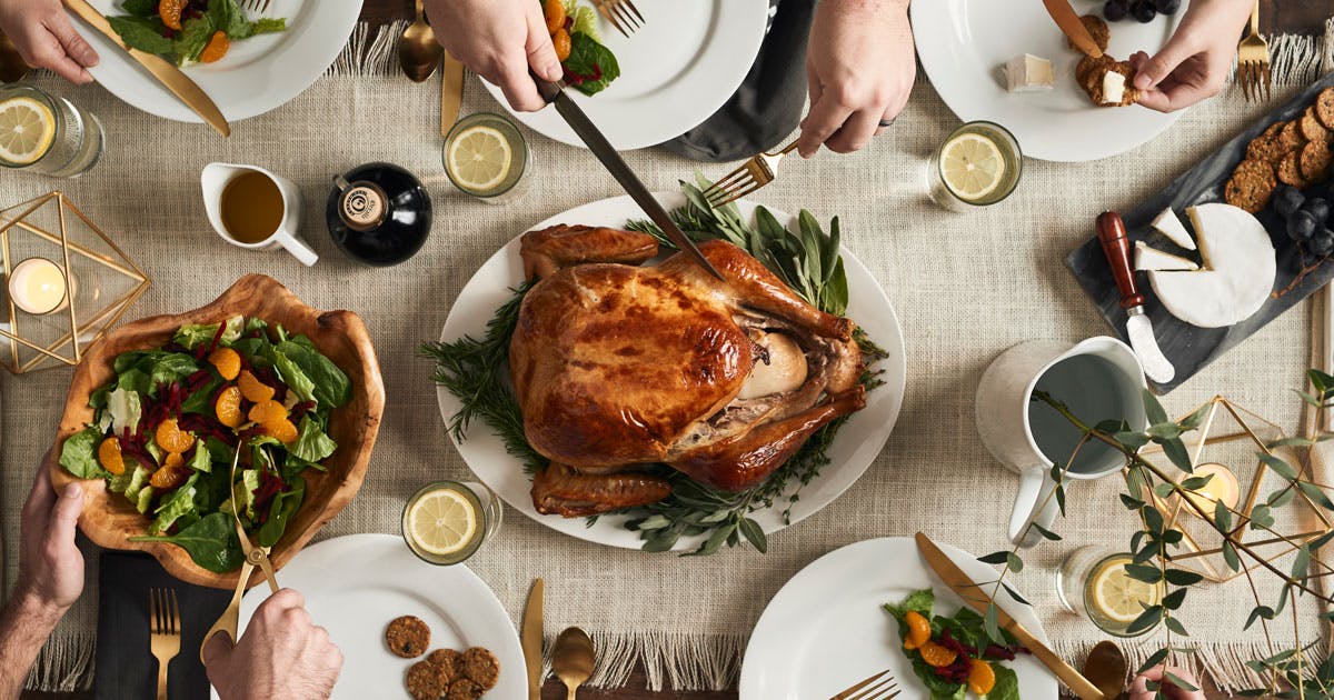 A birds-eye view of a roasted turkey and people gathered around a holiday table.