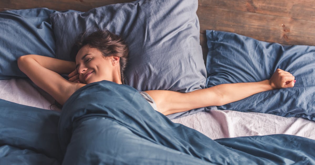 A smiling woman stretches as she lies in bed.