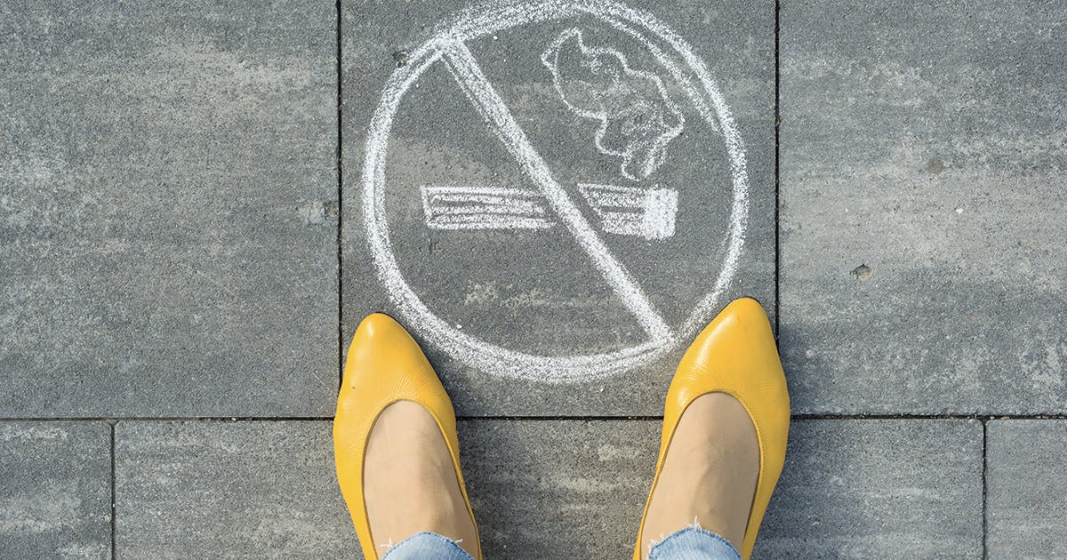 A woman is standing next to a no smoking symbol drawn on a sidewalk.