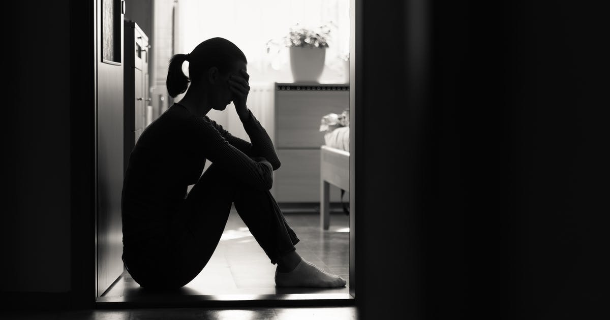 A woman silhouetted in a doorway, sitting on the floor with a hand to her eyes