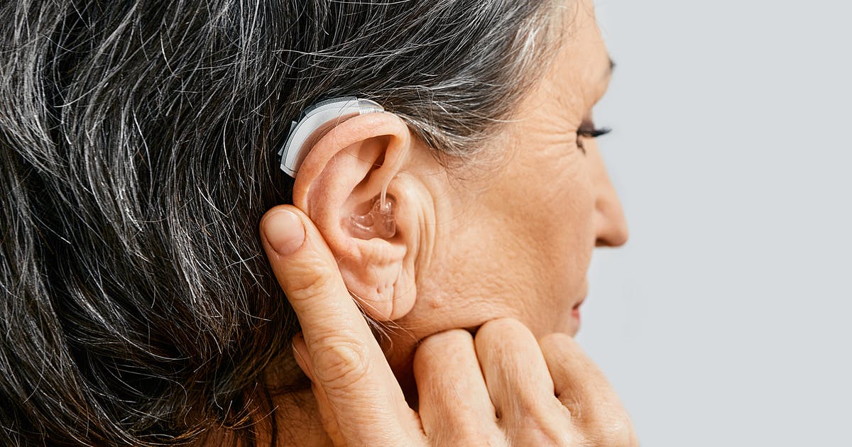 A woman points to her hearing aid.
