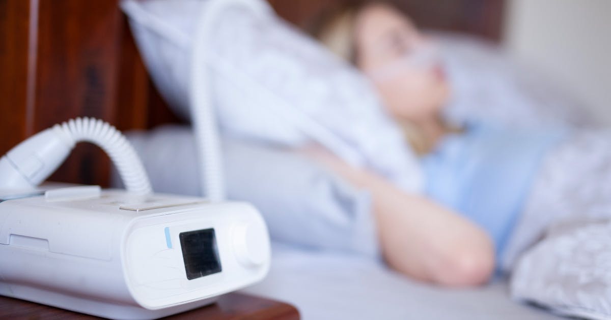 A CPAP machine in front of a person sleeping in bed.