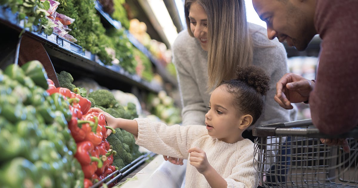 A young family shopping in the veggie section of a grocery store. 