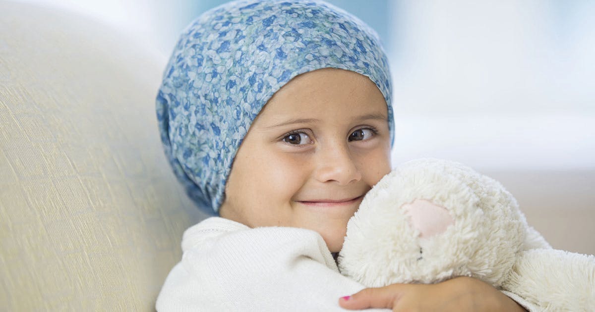A child battling cancer smiles while hugging a stuffed animal. 