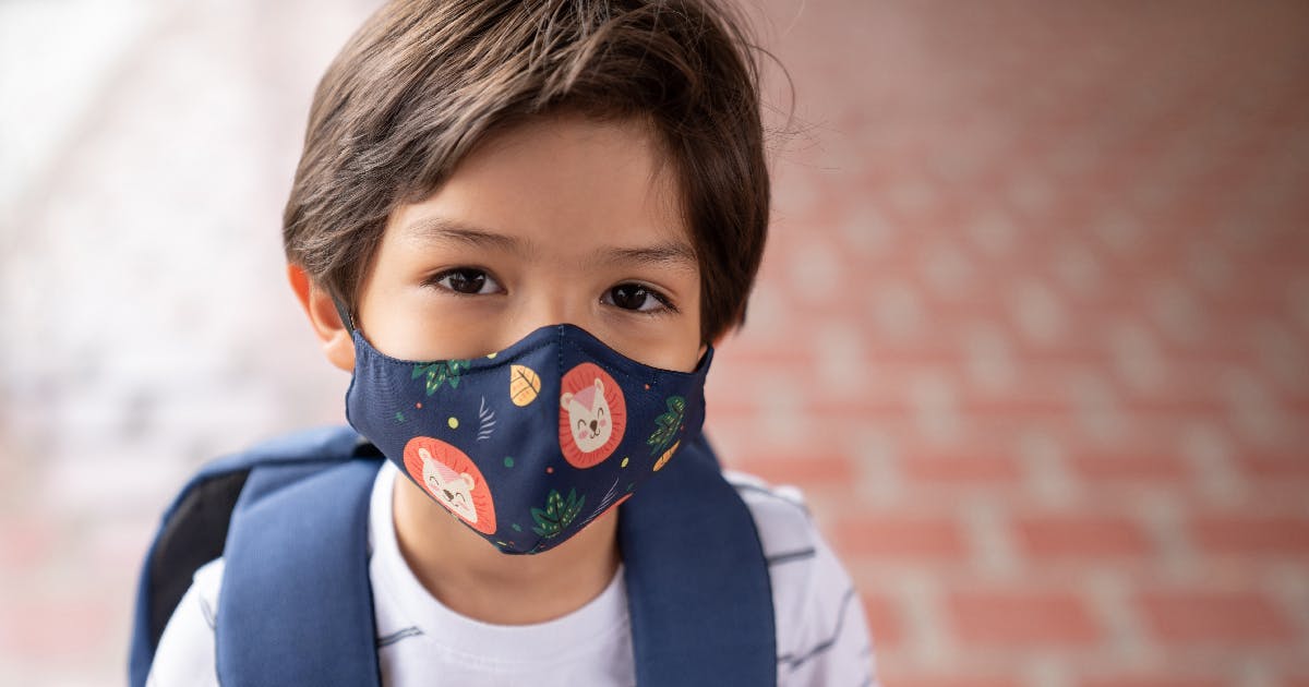 A young boy wearing a patterned mask and a backpack.