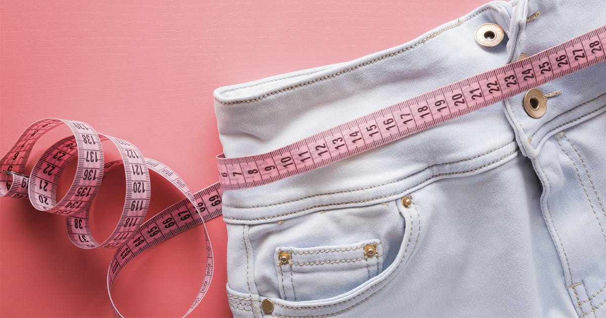 An empty pair of jeans surrounded by a tape measure at the waist. 