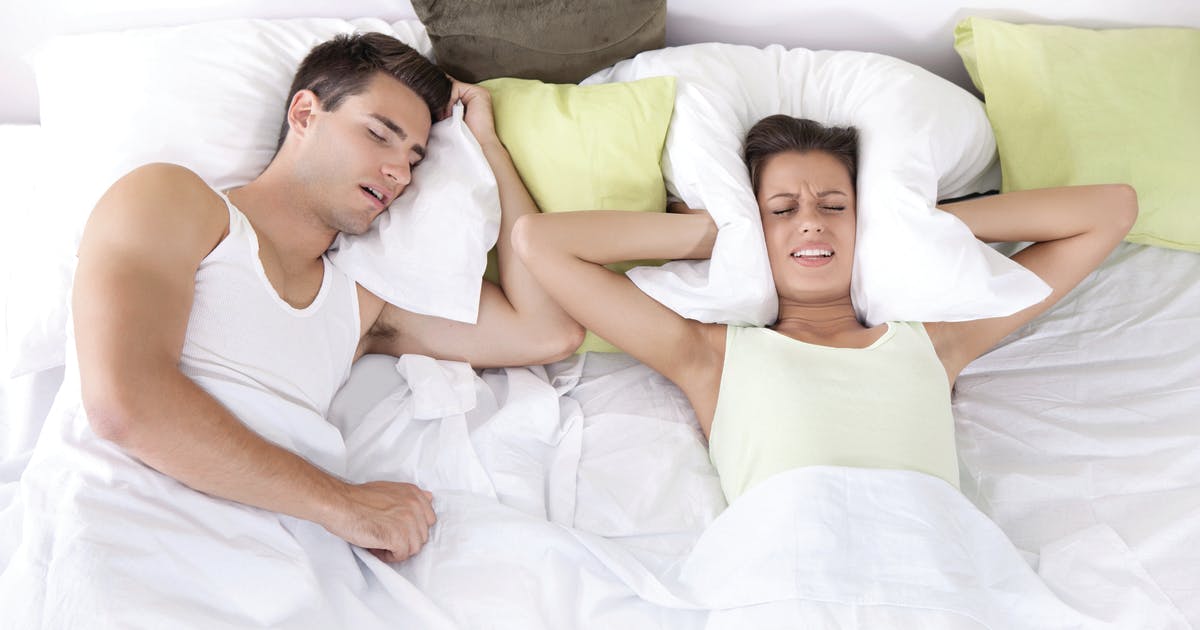 A man sleeps as a woman holds a pillow over her ears.