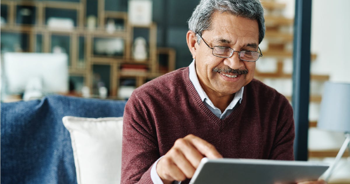 An older man smiles as he uses a tablet.