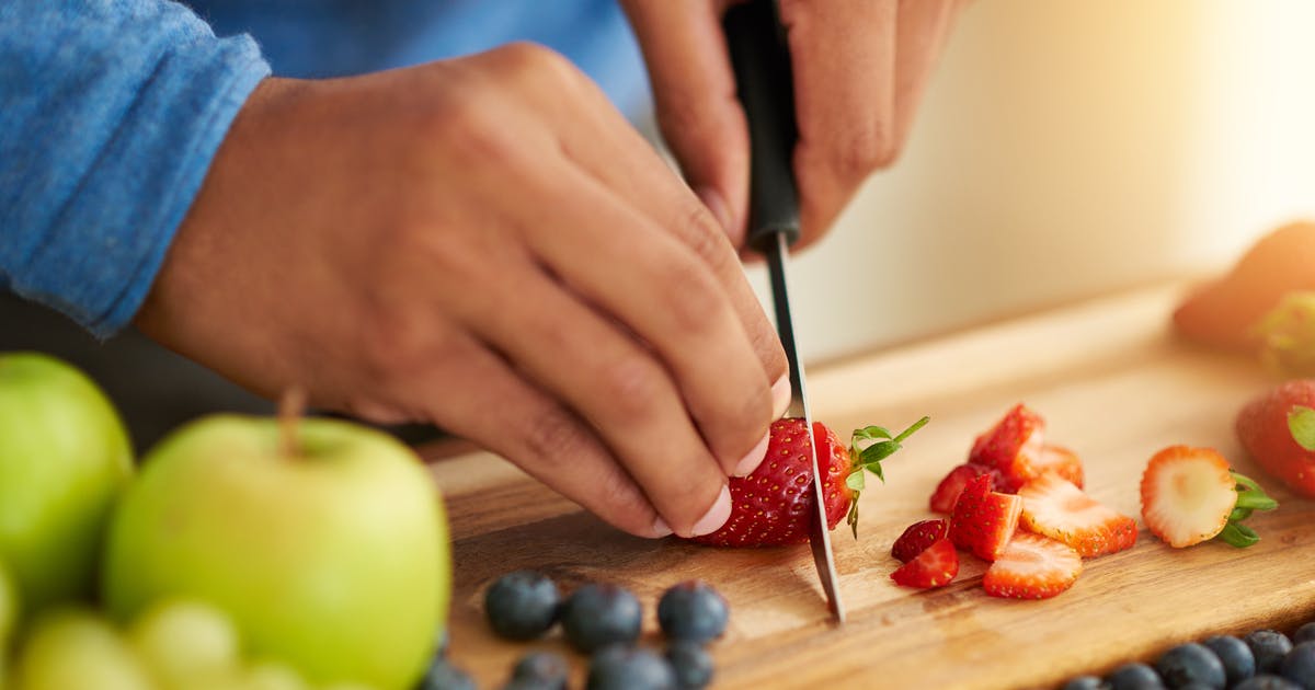Hands slice strawberries on a cutting board.
