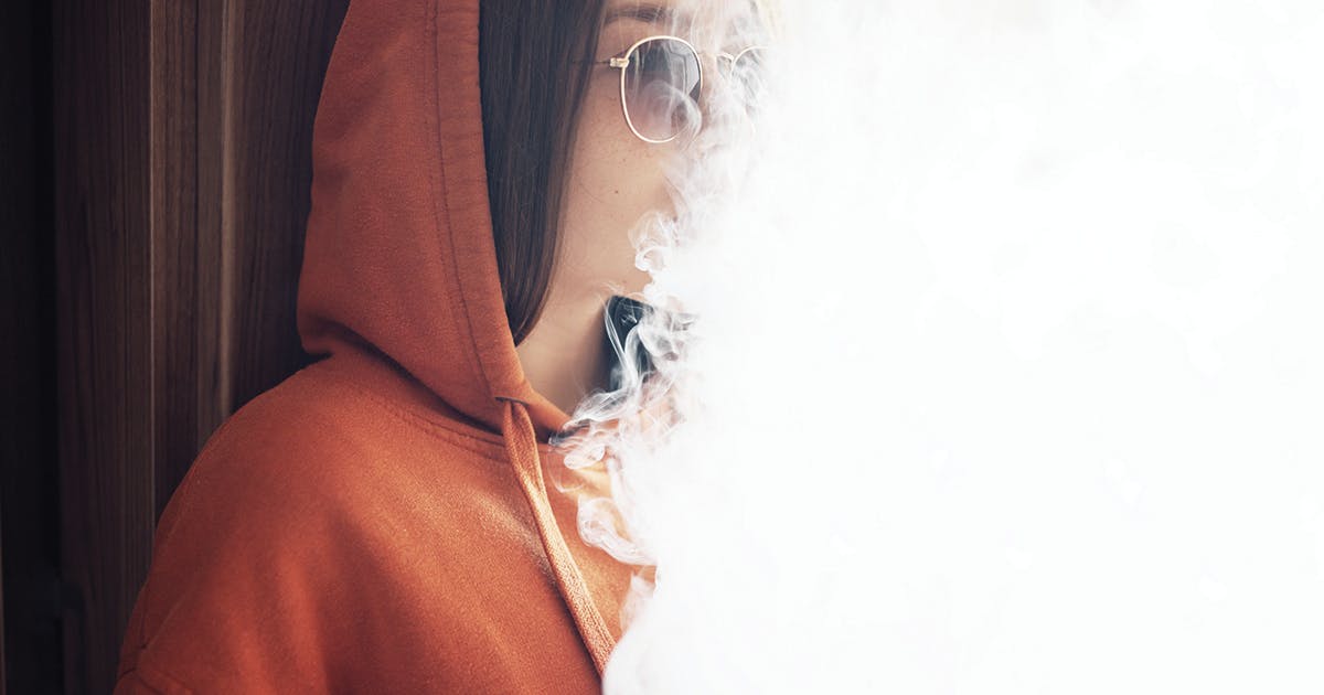 Young person in an orange hoodie obscured by smoke. 