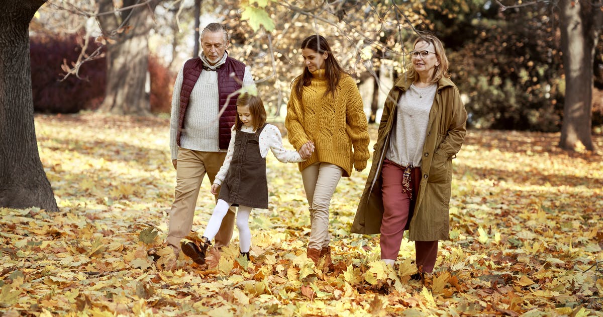 A multigenerational family walks through fall leaves.