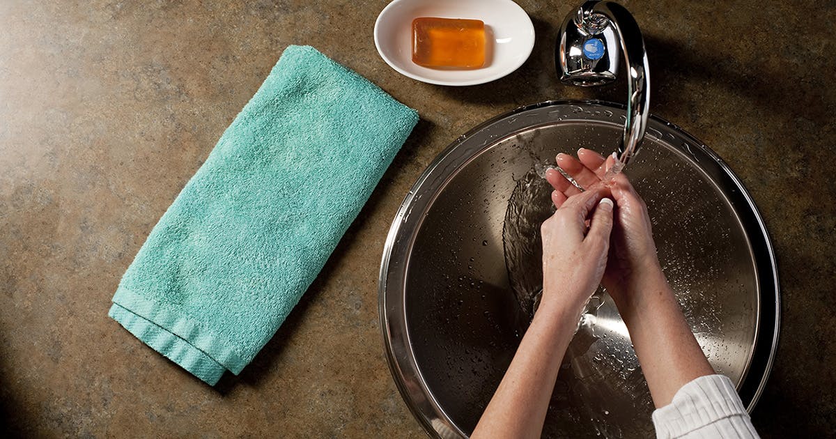 A woman washes her hands in a sink with a bar of soap and a hand towel nearby.