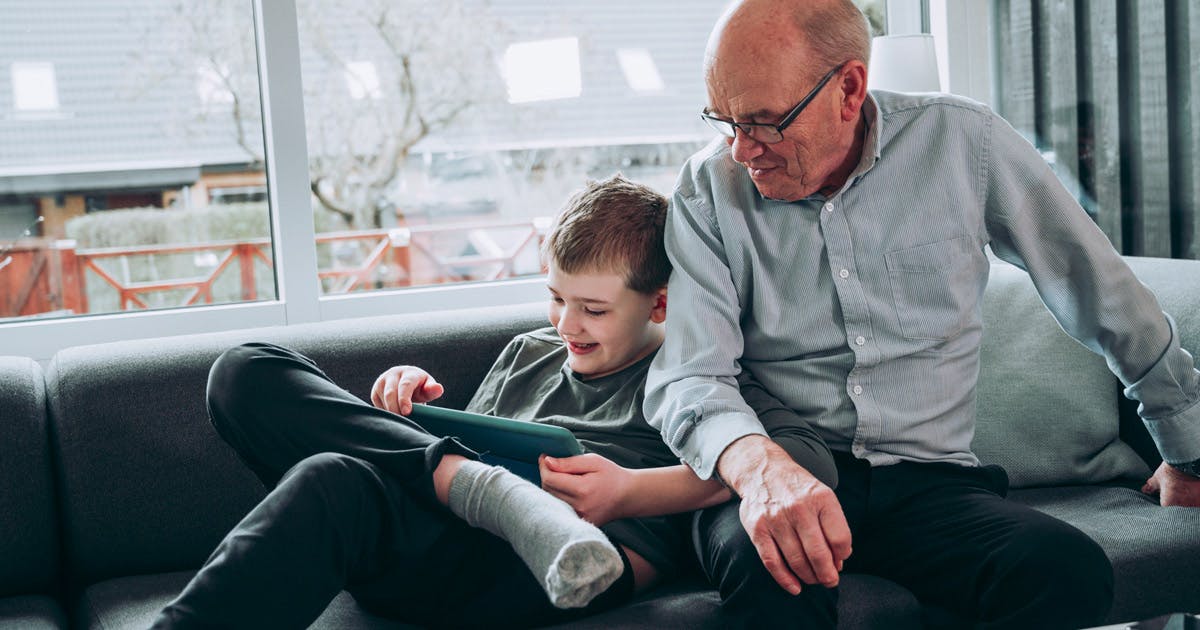 A grandfather and his grandson look at a tablet together.