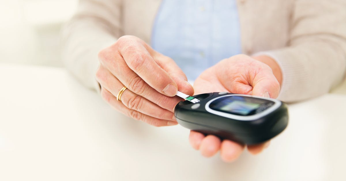 Hands insert a test strip into a glucose monitor.