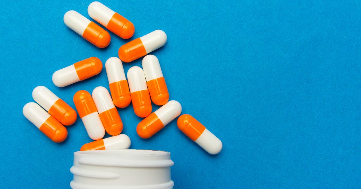Orange and white capsules spill from a white pill bottle.