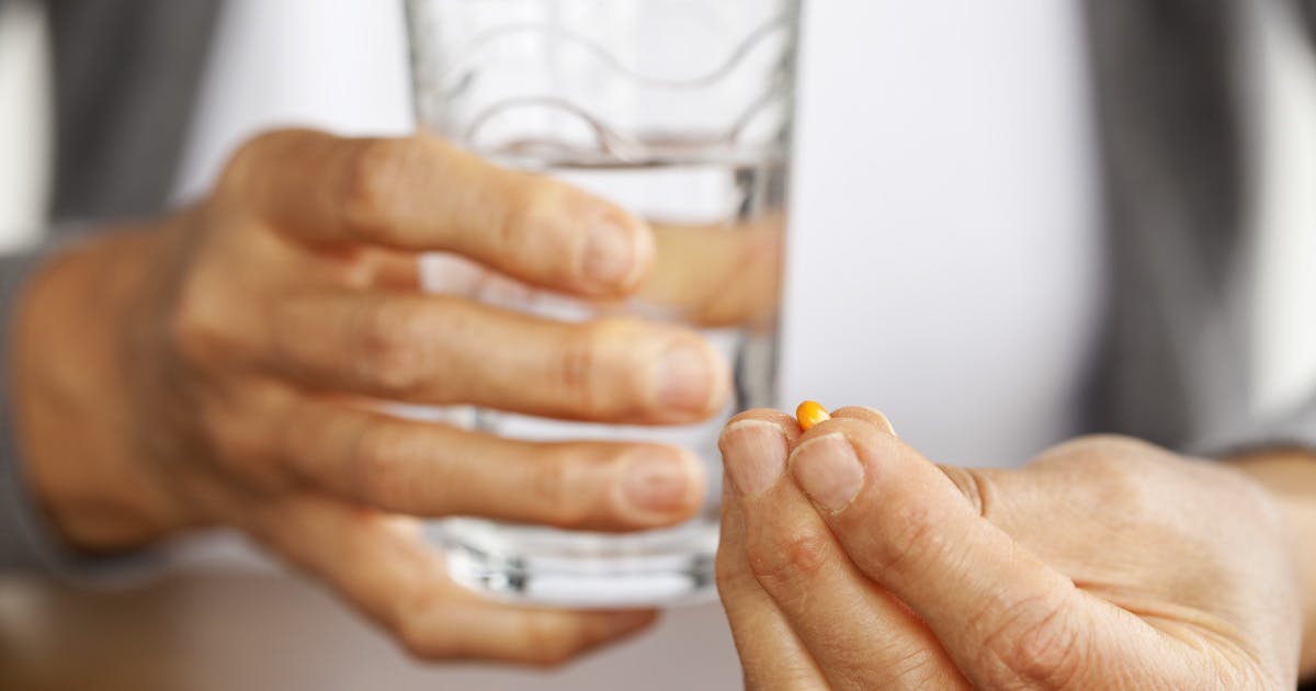 Person holding a glass of water and a pill in the other hand.