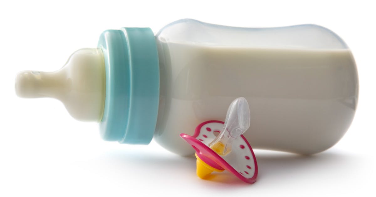 A full baby bottle on its side next to a pacifier.