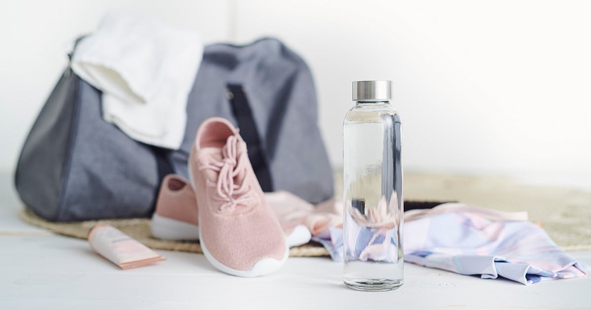A bottle of water in front of a gym bag, shoes, etc.