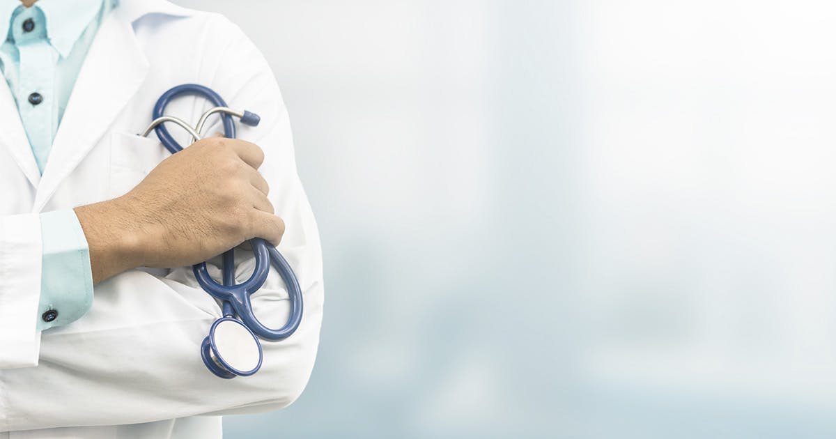 A close crop of a doctor in a white coat holding a blue stethoscope coiled in their hand. 