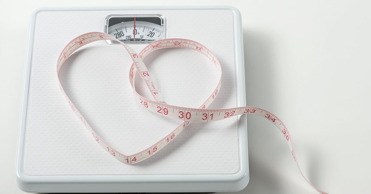 A bathroom scale with a tape measure forming a heart shape on it.