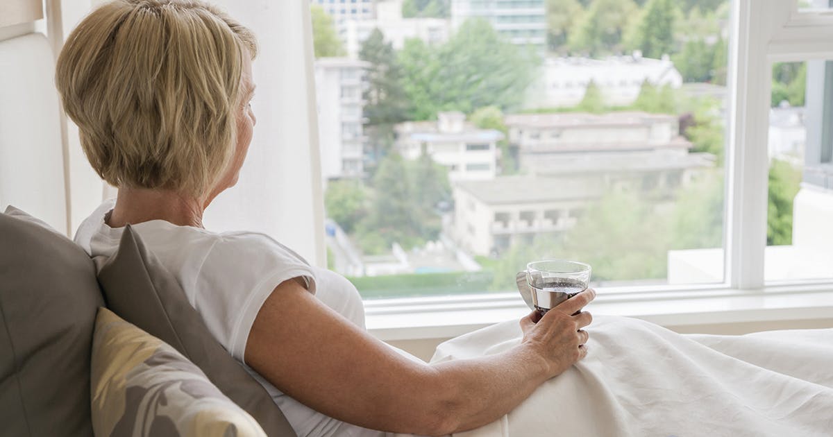 Woman with a cup of coffee sitting in bed looking out window 
