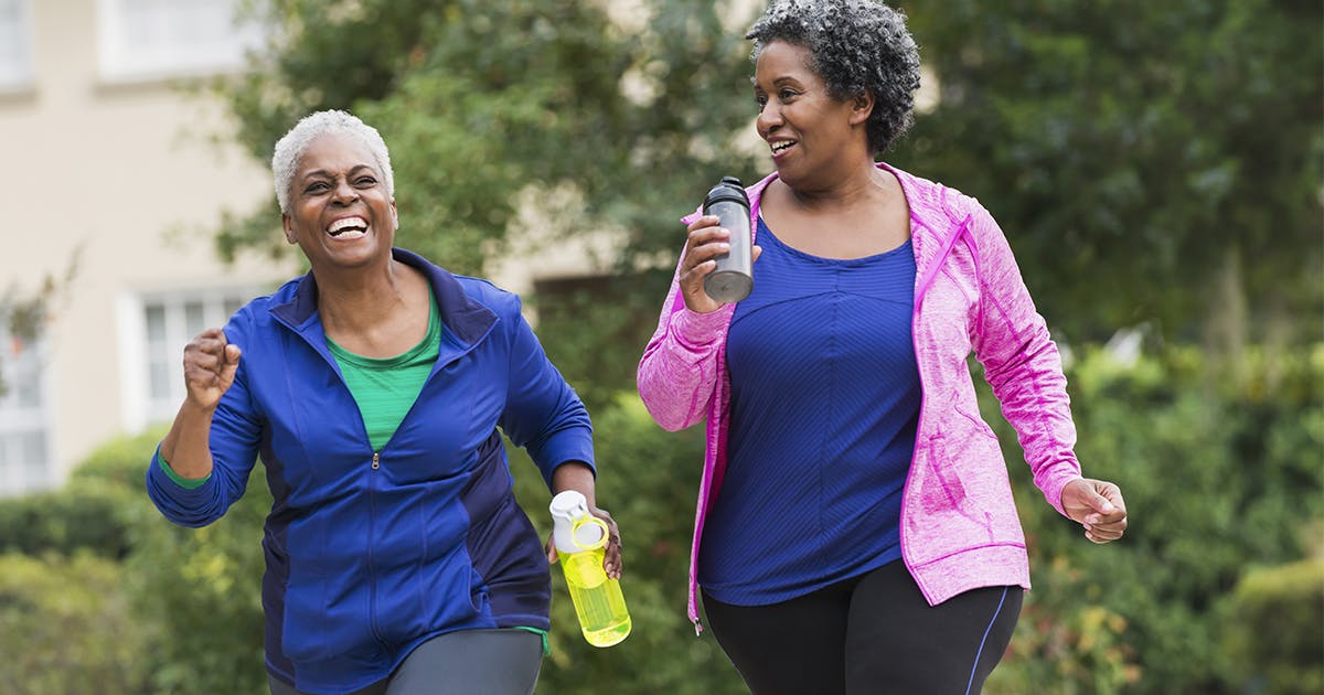 Two African American women in exercise clothes, walking down a street, holding water bottles.