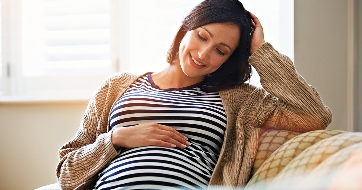 A pregnant woman smiling as she looks down and touches her belly.